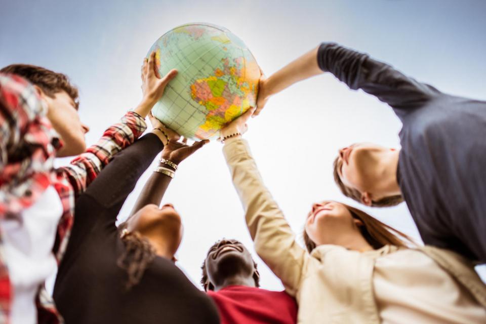 Five people place a hand on a globe positioned above their heads. 