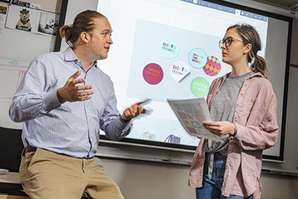 A faculty member stands next to a student in conversation.