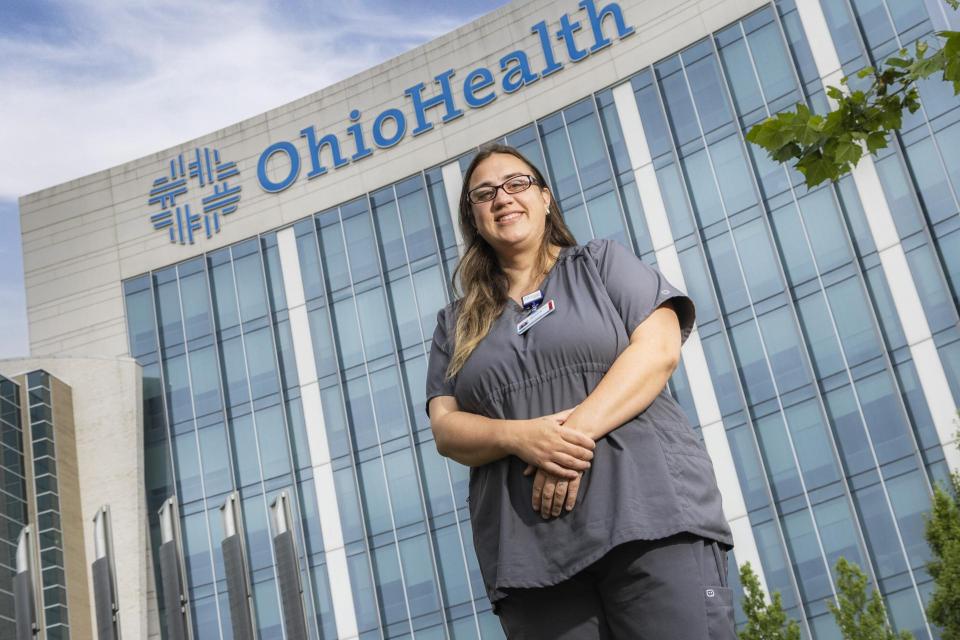 COTC alumna Jessica Kinser stands wearing scrubs in front of a medical building for OhioHealth where she works.