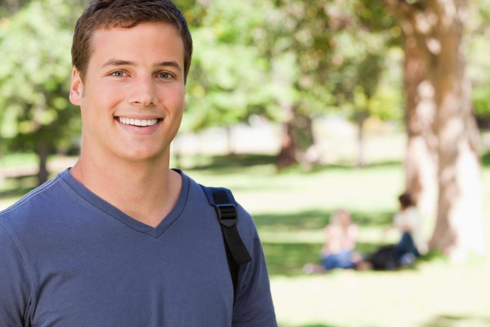Young man standing outside, smiling.