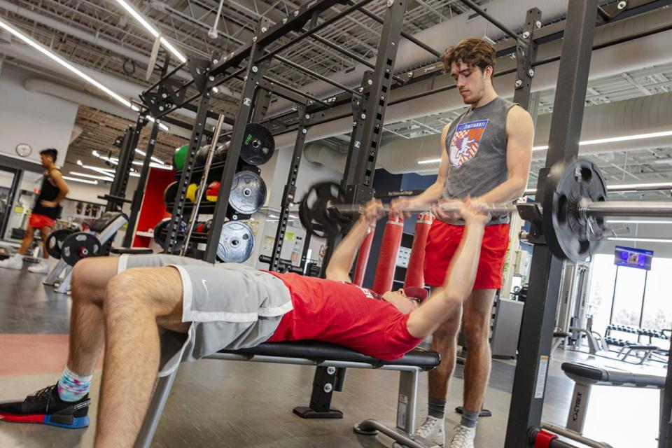 A student uses a bench press while another spots him. 
