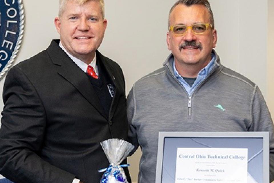 Man in suit and man with mustache wearing sweater holding framed certificate