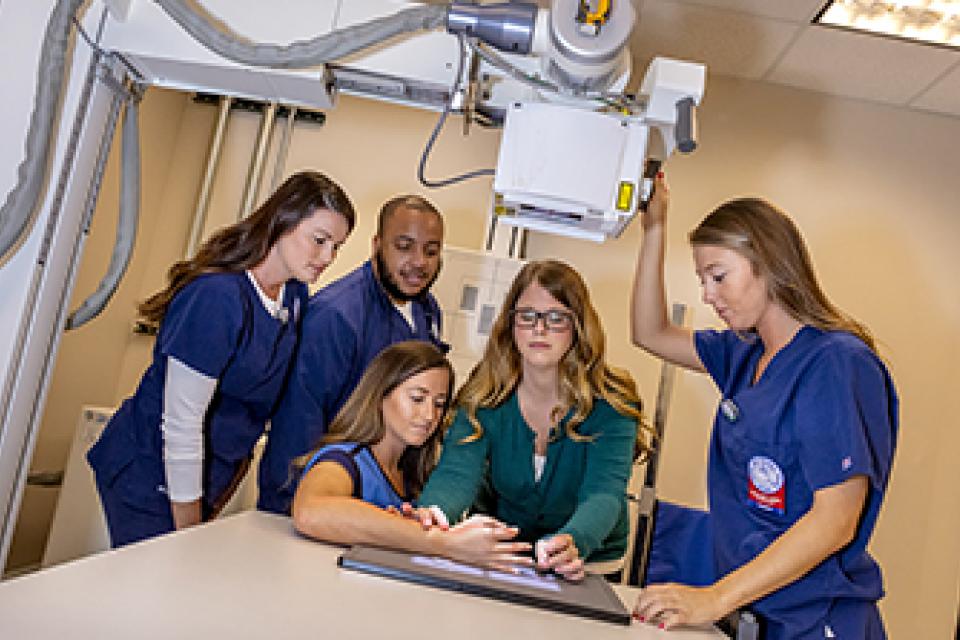 A professor helps assists a student in obtaining an x-ray while classmates stand by watching.