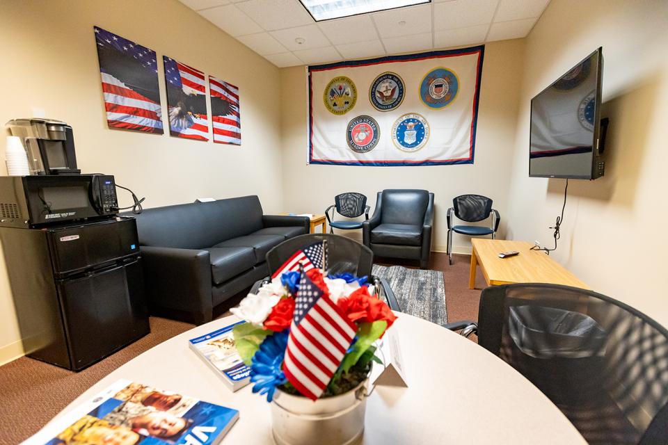 Inside the veteran's lounge are multiple seating areas with a couch and chairs, table, tv, refrigerator, microwave and coffee maker. 