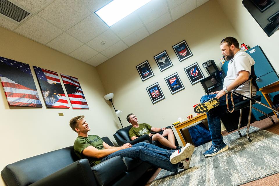 Three student veterans sit on chairs in the veterans lounge looking at each other in conversation.