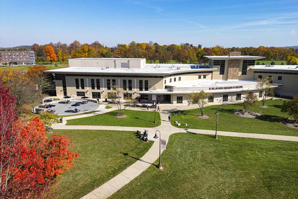 The exterior of the Warner Center from the backside where sidewalks lead to the door and trees are colored for autumn.