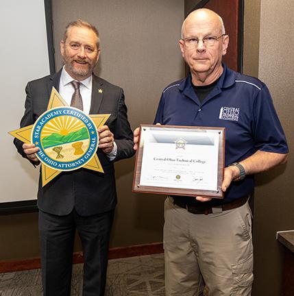 Man in suit holding star shaped sign next to man in polo shirt holding certificate