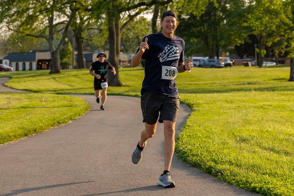 A man running on a path through campus gives a thumbs up.