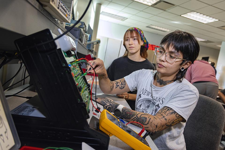 A student works with a piece of engineering equipment while another looks over their shoulder.