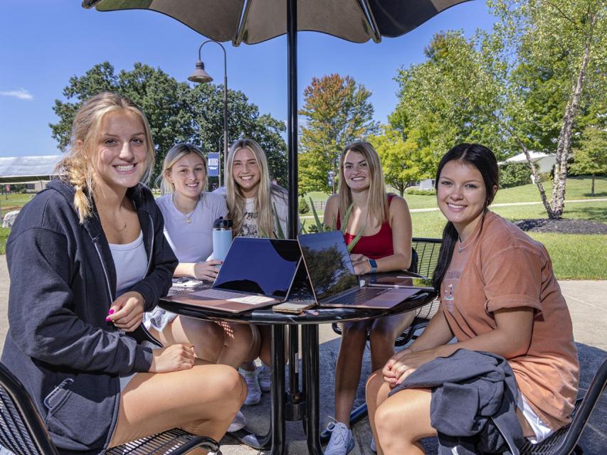 Five female students sit at a table outside on campus.