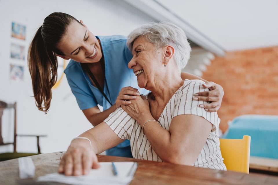 A young woman leans over with her hands around the shoulders of an older woman.