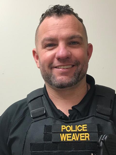 White male in bullet proof vest smiling at camera, COTC instructor and alumnus Jason Weaver