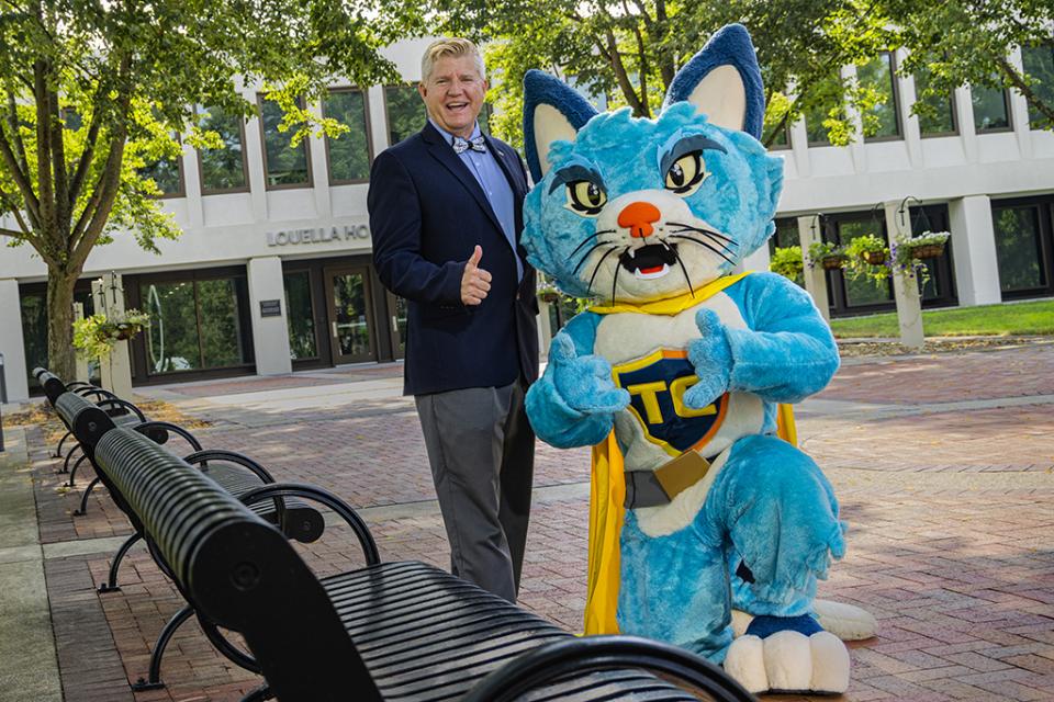 COTC President John M. Berry with COTC mascot TC the cat make "thumbs up" gestures outside of Louella Hodges Reese Hall on the COTC Newark campus.