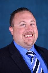 Man with dark hair in suit smiling at camera