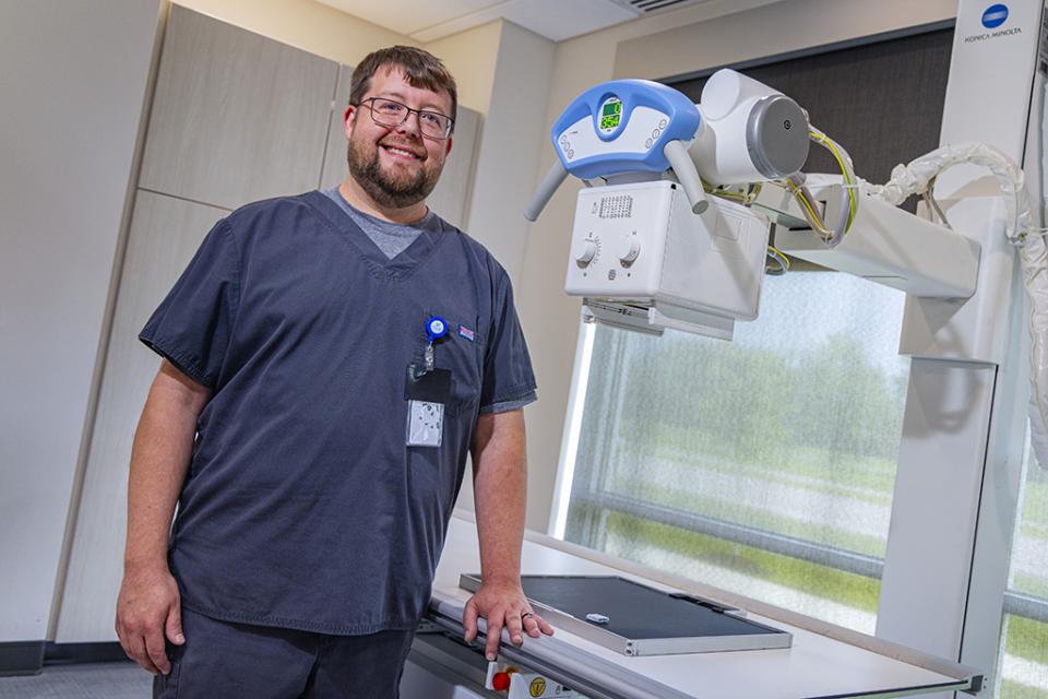 Shaun White wears scrubs and stands in front of an x-ray machine in COTC's radiologic science technology lab.