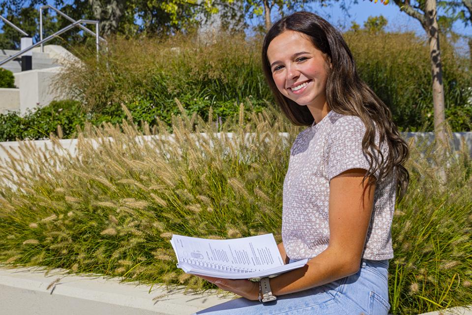 A student holding a book sits outside on the COTC Newark campus.