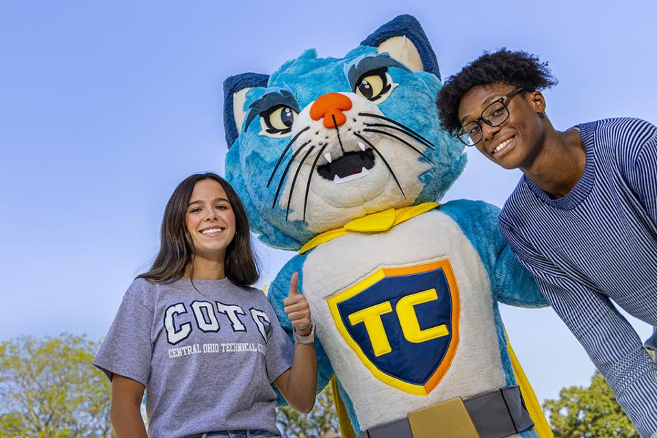 Two students stand, one holding up her index finger to say number one, on either side of TC the blue cat mascot of COTC.