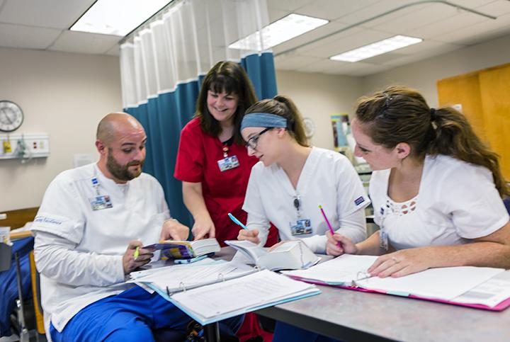 Three nursing students sit at a table  while Assistant Professor Susan Cooperider points to something in their notebook. 