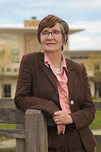 Older woman in brown suit leaning on bridge smiling at camera