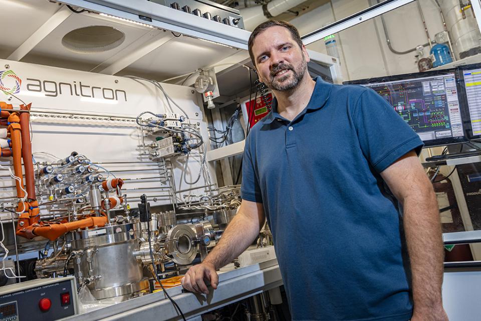 Travis Foster stands next to an agnitron semiconductor manufacturing equipment.